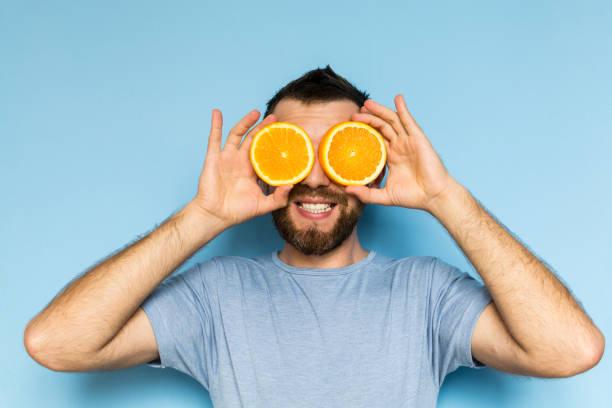 Young man holding slices of orange in front of his eyes stock photo