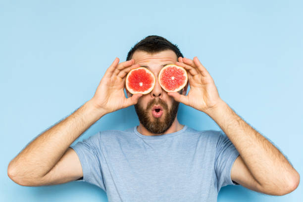 Young man holding slices of grapefruit in front of his eyes stock photo