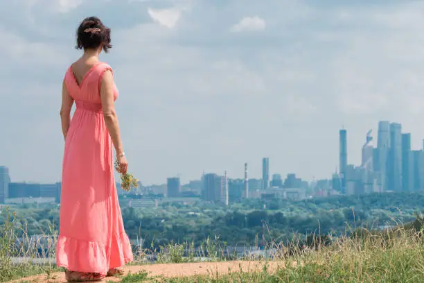 Concept - life in a big city and nature. A middle-aged woman looks at the city from a hill.
