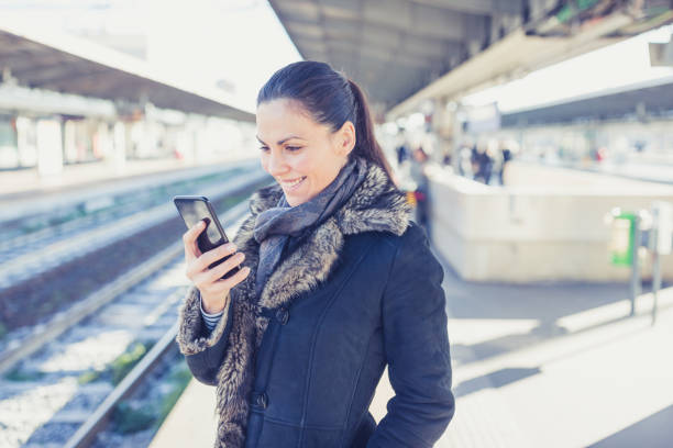 istock Young woman waiting on a train in a train station, she is using mobile phone 1007120540