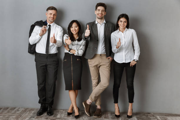 istock multicultural business people in formal wear showing thumbs up while standing at grey wall 1007144008