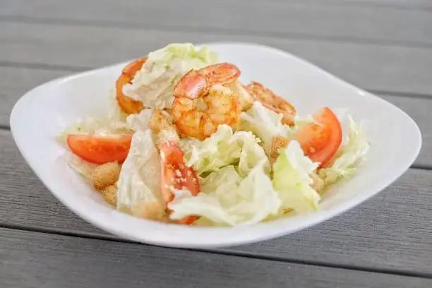 On a gray wooden table, a plate of food: dinner from Caesar salad with shrimps. side view