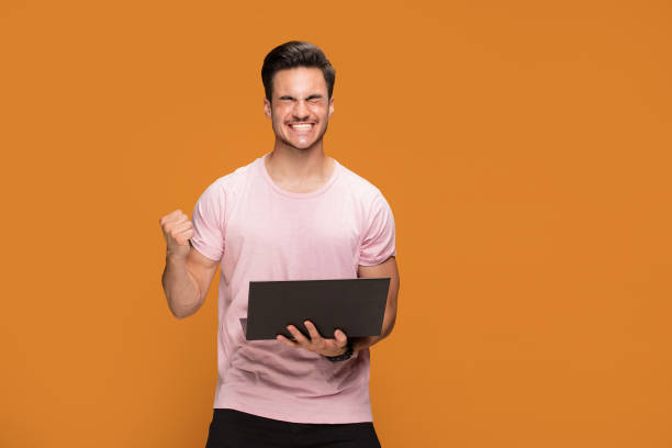 istock Happy young man with laptop on yellow background. 1007159764