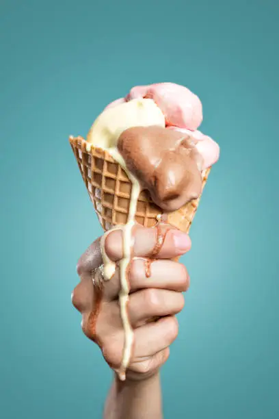 A hand is holding a large ice cream cone. The ice cream is melting down the hand.