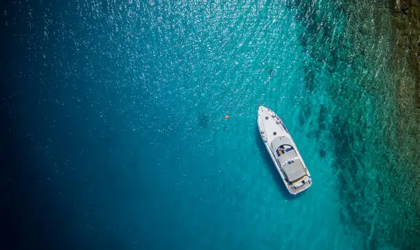 Luxury small yacht anchoring in shallow water, aerial view. Active life style, water transportation and marine sport.