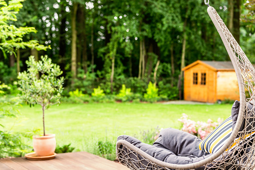 Hammock chair with striped cushion placed on terrace outside the house with garden