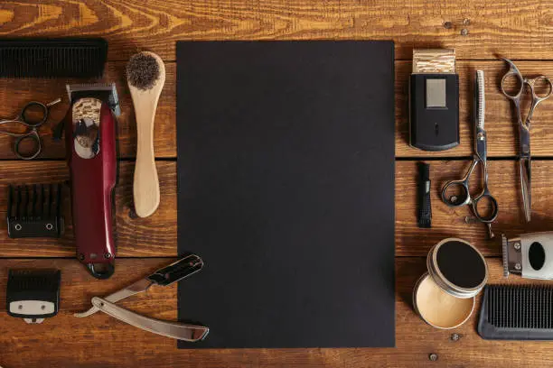 Photo of top view of professional barber tools and blank black card on wooden table