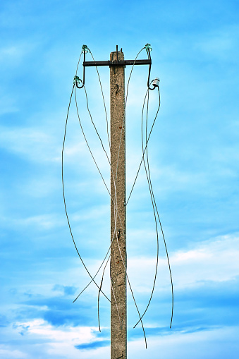 Old abandoned power line post with ripped electric wires hanging on it on the blue sky background
