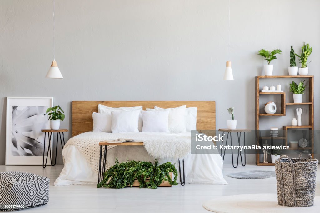 Patterned pouf and basket in bright bedroom interior with lamps, plants and poster next to bed. Real photo Bedroom Stock Photo