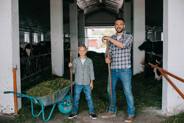 istock father and son holding pitchforks and smiling at camera while working together in stall 1007188984