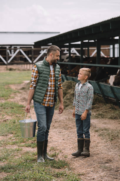 istock father with bucket and little son in rubber boots looking at each other while working together at ranch 1007189020