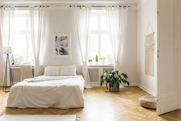 istock Poster between windows in bright bedroom interior with bed between plant and lamp. Real photo 1007194078