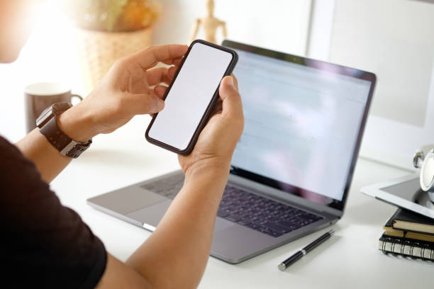 istock Cropped shot of man using mobile phone while working with laptop on desk. 1007194972