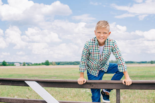 istock happy boy climbing on fence and smiling at camera on farm 1007195070