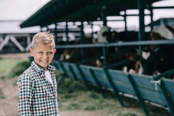 istock happy boy in checkered shirt smiling at camera while standing at ranch with cows 1007195082