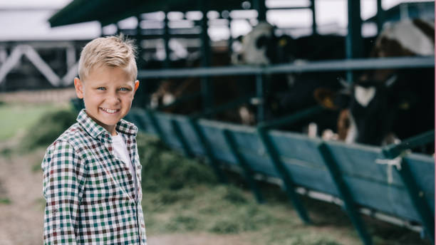 istock boy in checkered shirt smiling at camera while standing at ranch with cows 1007195088