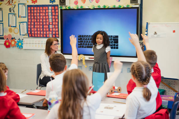 Presenting to her Classmates with her Teacher An elementary schoolgirl presents her work to the class with the support of her teacher beside her. This is a school in Hexham, Northumberland in north eastern England. kids using smart board stock pictures, royalty-free photos & images