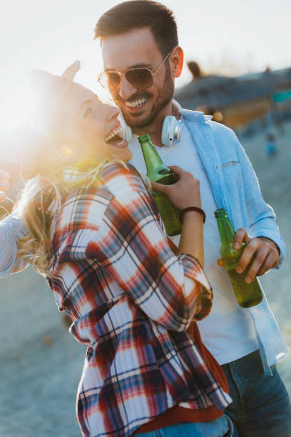 istock Happy couple smiling and drinking beer at beach 1007225714