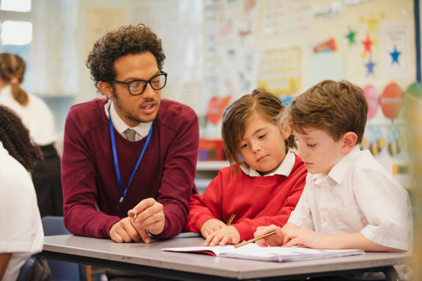 Schoolboys Work with their Teacher in Elementary Class Two schoolboys work through a textbook with their teacher in elementary class. This is a school in Hexham, Northumberland in north eastern England. instructor stock pictures, royalty-free photos & images