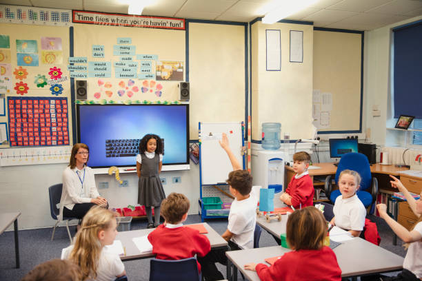 Presenting to the Class with her Teacher An elementary schoolgirl presents her work to the class with the support of her teacher beside her. This is a school in Hexham, Northumberland in north eastern England. kids using smart board stock pictures, royalty-free photos & images