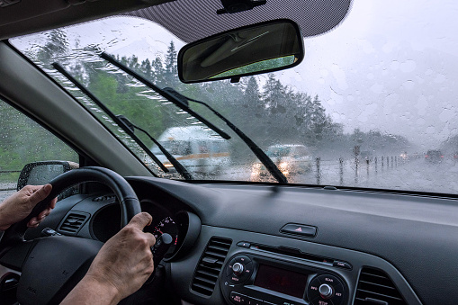 View through the rain-drenched windshield. Driver's hands and part of the car interior