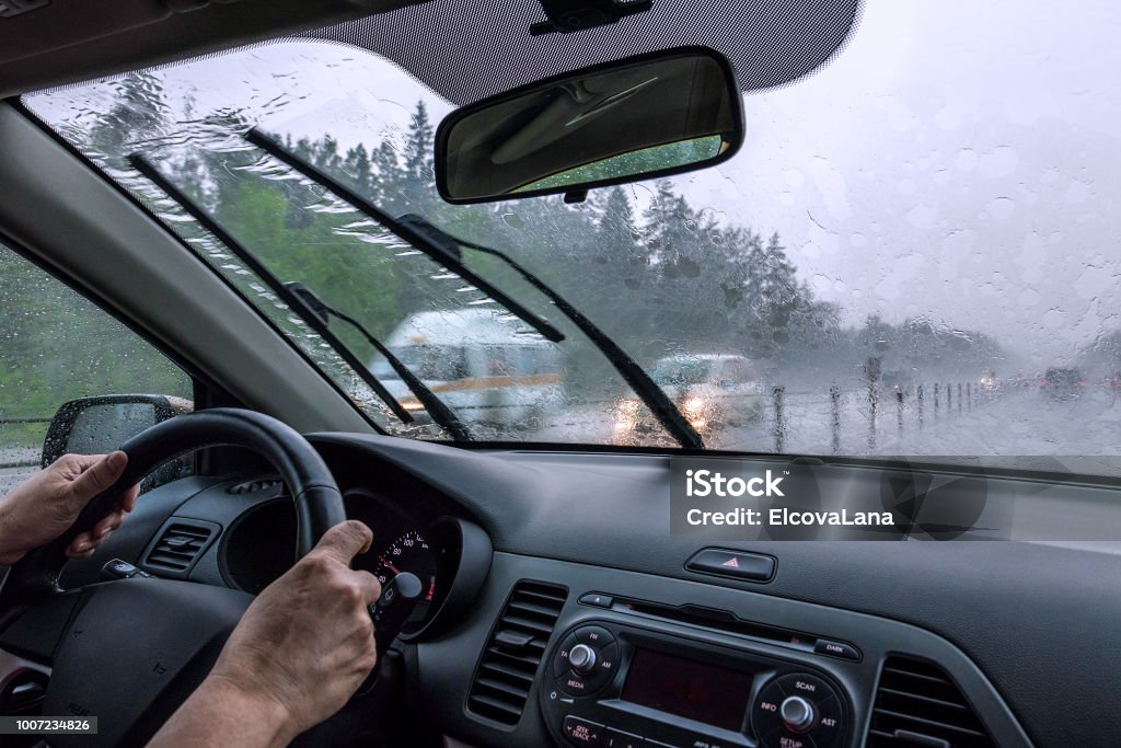 View through the rain-drenched windshield. Driver's hands and part of the car interior Blurred silhouettes of vehicles. Inside view of the car Rain Stock Photo