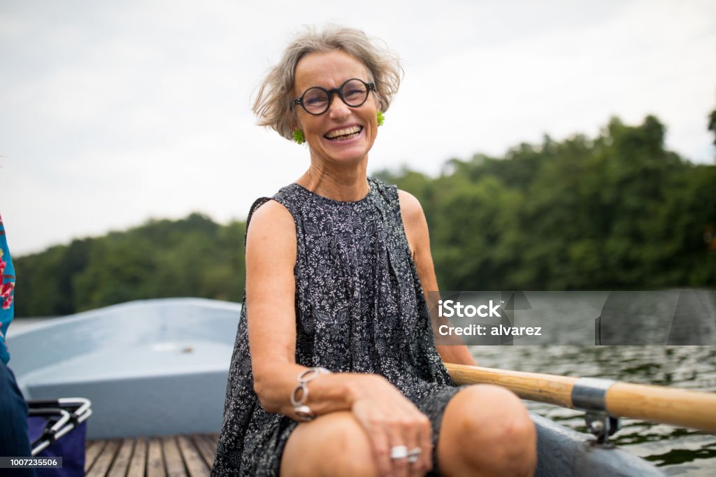 Smiling mature woman sitting on rowboat in lake Portrait of smiling mature woman sitting on rowboat. Happy female is enjoying boating in lake at forest. She is on vacation. Mature Women Stock Photo