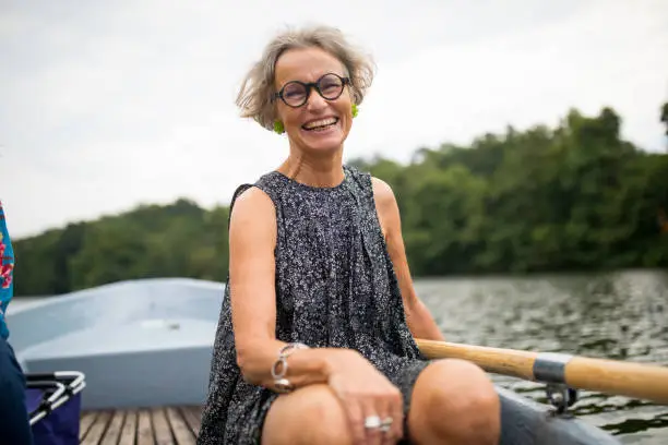 Portrait of smiling mature woman sitting on rowboat. Happy female is enjoying boating in lake at forest. She is on vacation.