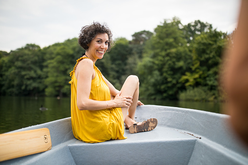 Portrait of mature woman sitting on rowboat in lake. Happy female is enjoying vacation in forest. She is wearing casuals while boating.