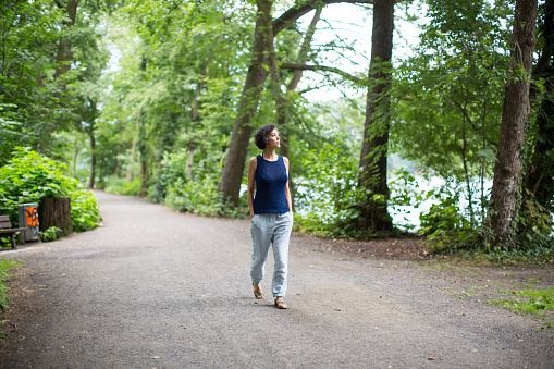 Mature woman walking on road in forest. Full length of female is exploring while hiking in woods. She is wearing casuals.