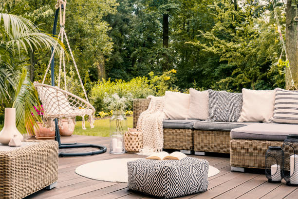 réservez sur un pouf noir et blanc au milieu d’une terrasse lumineux avec un canapé d’angle en rotin, chaise accrochante et tour de tapis. vraie photo - furniture photos et images de collection