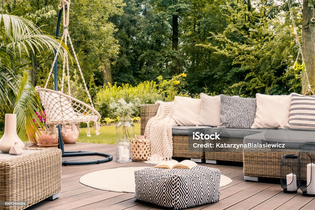 Book on a black and white pouf in the middle of a bright terrace with a rattan corner sofa, hanging chair and round rug. Real photo Yard - Grounds Stock Photo