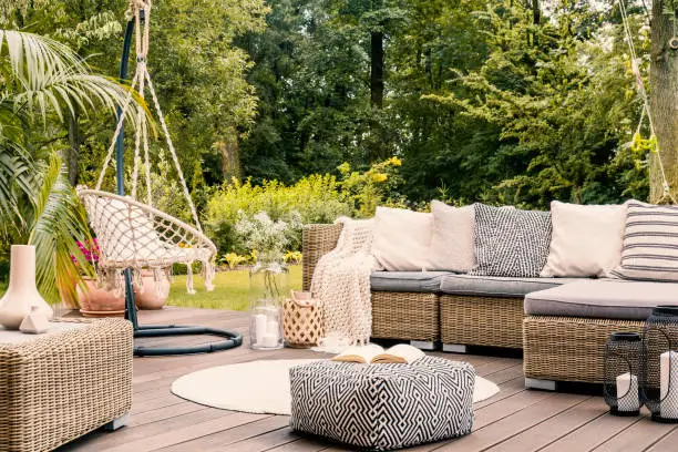 Photo of Book on a black and white pouf in the middle of a bright terrace with a rattan corner sofa, hanging chair and round rug. Real photo