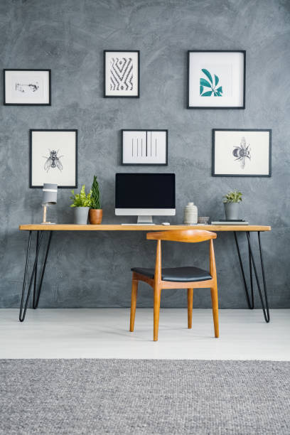 istock Wooden chair at desk with computer desktop against grey wall with posters in workspace interior. Real photo 1007250710