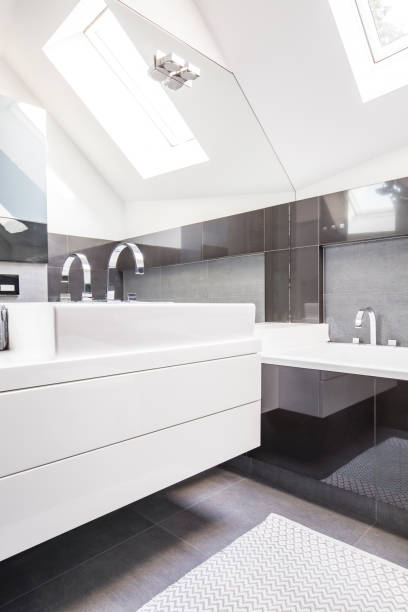 istock Big mirror by a modern, white washbasin cabinet in a fancy bathroom interior with reflective, black tiles and a roof window 1007254302