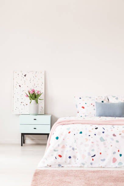 istock Flowers on pastel cabinet next to patterned bed with blue pillow in white bedroom interior. Real photo 1007254988
