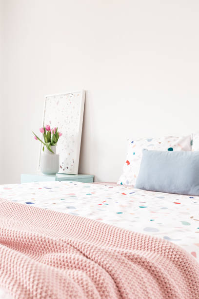 istock Pink blanket on bed with patterned sheets and blue cushion in bedroom interior with flowers. Real photo 1007255000