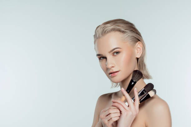 istock beautiful blonde girl holding makeup brushes, isolated on grey 1007258076