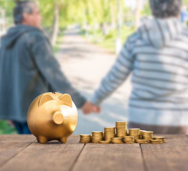 Retirement savings Piggy bank and gold coins on a table in front of an elderly couple holding hands physical gold ira stock pictures, royalty-free photos & images