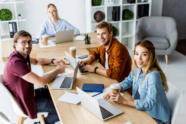 istock high angle view of smiling multicultural colleagues working on startup project in office and  looking at camera 1007294120