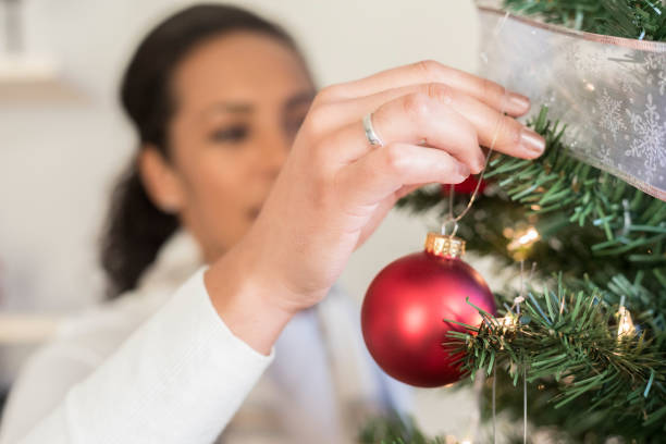 This is a closeup of a Christmas ornament as it is hung on a Christmas tree by a woman in her home.