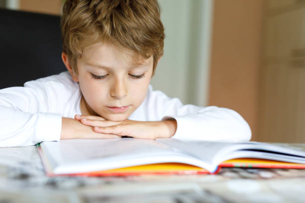 istock Little blonde school kid boy reading a book at home 1007304618