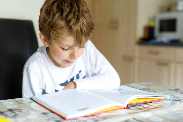 istock Little blonde school kid boy reading a book at home 1007304846