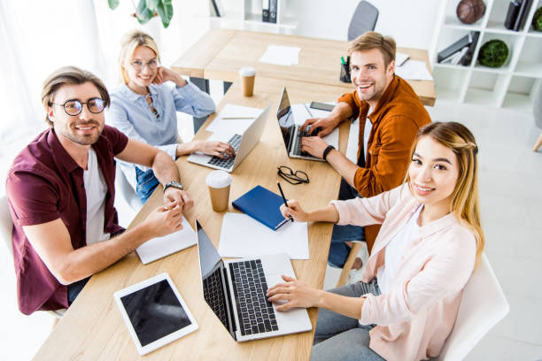 istock high angle view of multicultural colleagues working on startup project in office with gadgets and looking at camera 1007305024