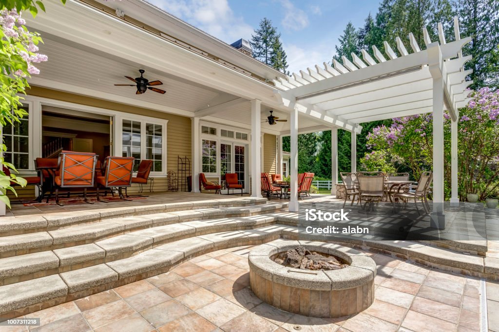Lovely outdoor deck patio space with white dining pergola. Lovely outdoor deck patio space with white pergola, fire pit in the backyard of a luxury house. Pergola Stock Photo