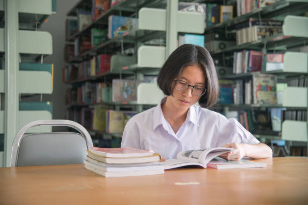 istock Asian student girl reading book in public library 1007313936