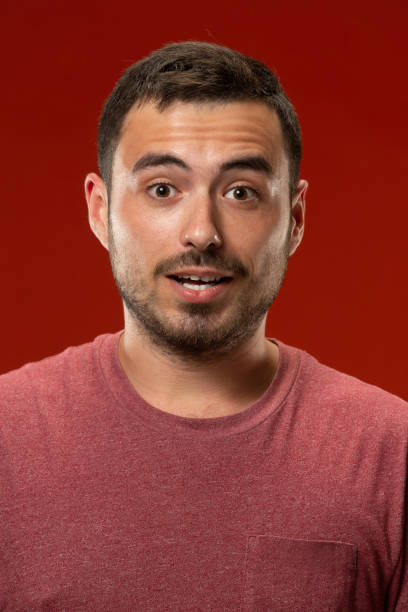 istock The young attractive man looking suprised isolated on red 1007326710