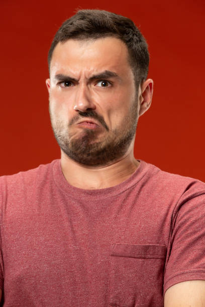 istock The young emotional angry man screaming on red studio background 1007329388