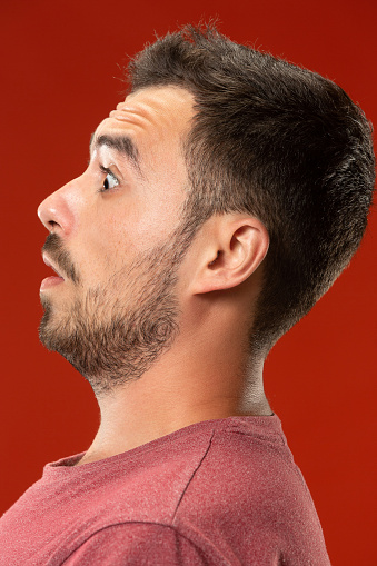 Wow. Attractive male half-length front portrait on red studio backgroud. Young emotional surprised bearded man standing with open mouth. Human emotions, facial expression concept. Trendy colors