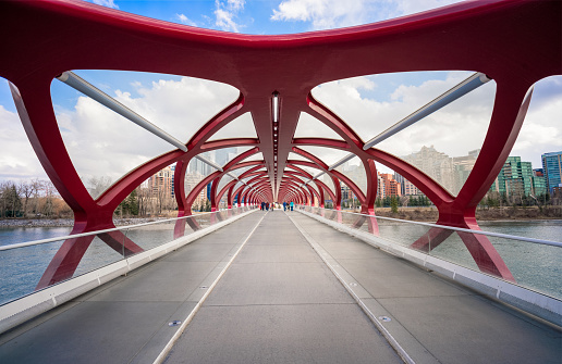 Calgary, Canada - A wide angle view of the unusual design of the Peace Bridge across the Bow River in Calgary, with pedestrians and cyclists crossing the bridge in the distance. The bridge was designed by Santiago Calatrava, and opened in 2012.